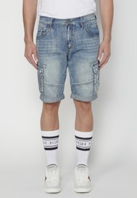 Valkobla denim cargo shorts med flera fickor, rullad fåll och synliga sömdetaljer. I kombination med vita strumpor med svarta ränder.