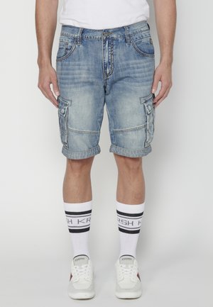Lichtblauwe denim cargoshorts met meerdere zakken, omgeslagen zoom en zichtbare stiksels. Gecombineerd met witte sokken met zwarte strepen.