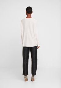 Krämfärgad stickad tröja, avslappnad passform, mjuk textur. Svarta läderbyxor med knappdetalj vid fållarna. Ormskinnsmönstrade klackar synliga.