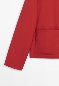 Red jacket with a smooth texture, featuring a pocket on the front and a structured sleeve design. Material appears lightweight and durable.