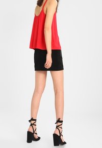 Haut sans manches rouge avec un dos texturé, associé à une mini jupe en daim noire et des sandales à talons hauts noires à lanières.