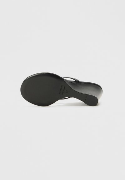 Sandale noire à talons hauts avec un dessus en cuir lisse, des lanières fines et un bout arrondi. Présente une semelle noire unie avec un logo subtilement embossé.