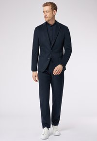 Completo a righe navy realizzato in tessuto testurizzato, dotato di una giacca sagomata con due bottoni, abbinato a pantaloni coordinati e sneakers bianche.