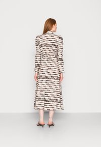 Vestido de manga longa, estampado em tons de bege e castanho, com cintura elástica e uma silhueta fluida, apresentando um comprimento até à meia-canha.