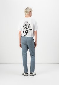 Biała koszulka z czarnym graficznym wzorem na plecach, zestawiona z jasnoniebieskimi spodniami i czarno-białymi sneakerami. Minimalistyczny, czysty wygląd.