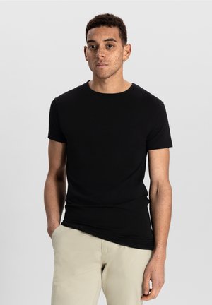 T-shirt noir à manches courtes en tissu léger et lisse. Caractéristiques : col rond classique et coupe décontractée, associé à un pantalon beige clair.