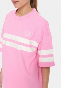 T-shirt in cotone rosa con strisce orizzontali bianche. Presenta un collo rotondo e una piccola stampa grafica sul petto. Vestibilità rilassata.
