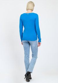 Maglione azzurro a maglia con maniche lunghe, orlo a coste e scollatura ampia, abbinato a jeans azzurri chiari e stivali neri con tacco alto.