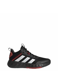 Zapatillas deportivas negras con parte superior de malla texturizada, rayas blancas y acentos rojos. Presentan una suela de goma gruesa y con patrón, y una lengüeta para facilitar el calzado.