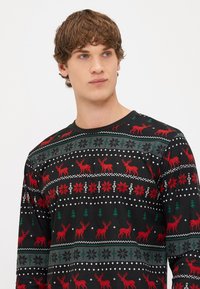 Long-sleeve black sweater featuring red reindeer, snowflakes, and trees in a repeated festive pattern. Soft fabric with a crew neckline.
