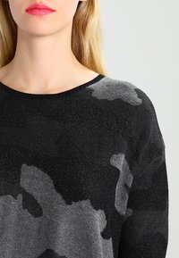 Černý a šedý svetr s maskáčovým vzorem a kulatým výstřihem, vyrobený z texturované příze, která dodává jemný lesk. Měkký, pohodlný materiál.