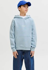 Sweat à capuche bleu clair avec poche avant et logo brodé, associé à un jean ample bleu foncé. La casquette ajoute un accent bleu contrastant.