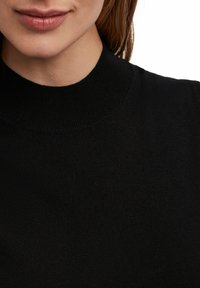 Zwarte gebreide trui met een hoge, geribbelde halslijn, een gladde textuur en een aansluitend design. Close-up van de kraag en het borstgebied.