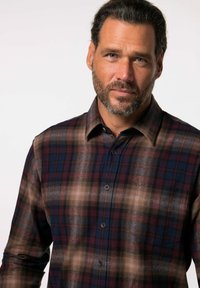 Camisa de cuadros en tonos marrón, marino y burdeos. Diseño abotonado con collar abierto y bolsillo en el pecho. Tejido suave y texturizado.