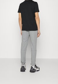 Svart t-shirt i bomull, grå sweatpants och kraftiga svarta och vita sneakers. Klädseln har en avslappnad passform med elastiska midjeband.