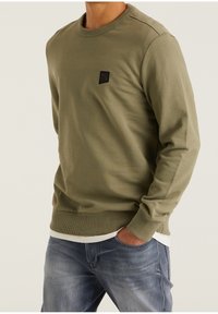 Sudadera verde oliva hecha de tejido texturizado, con un escote redondo y un pequeño parche de logo negro en el pecho. Diseño de corte clásico.