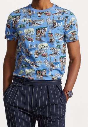 Blå T-shirt med detaljerede tryk af bamser i parisscener, kombineret med marineblå bukser med smalle striber og et armbåndsur med brun læderrem.