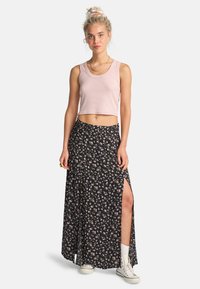 Lys rosa kort tanktop parret med en sort blomster maxi-nederdel med sideslids. Modellen bærer hvide sneakers og ankelsokker.