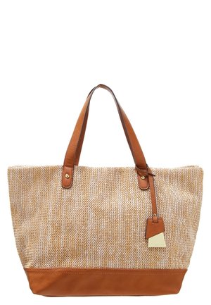 Grand sac cabas tissé beige avec des poignées en cuir marron, une base et une étiquette en cuir pendue à une poignée.