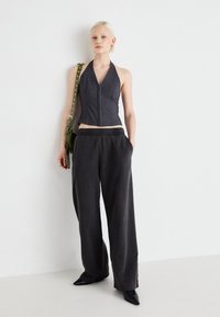 Grå halterneck crop top med forside lynlås, parret med grå løstsiddende bukser med elastisk talje og sidelommer. Sorte spidse sko.