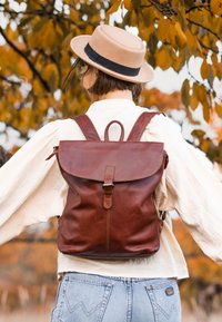 Smeđa kožna ruksak s preklopnikom, podesivim trakama i gornjom drškom. Teksturirana površina s naglaskom na kopči. Neformalni dizajn.