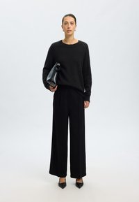 Pulover negru tricotat cu un guler rotund, asortat cu pantaloni largi negri. Ține în mână o geantă de mână neagră; tocuri negre cu vârful pătrat. Design simplu și elegant.