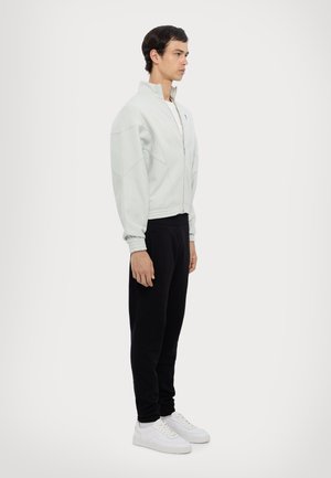 Giacca zip-up grigia chiara con colletto alto, polsini elasticizzati, abbinata a pantaloni neri e sneakers bianche, caratterizzata da una vestibilità moderna e rilassata.