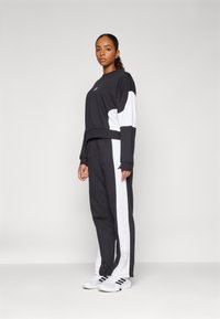 Conjunto atlético em preto e branco com um suéter cropped e calças jogger com riscas laterais em contraste. O material parece suave e a fit é descontraída.