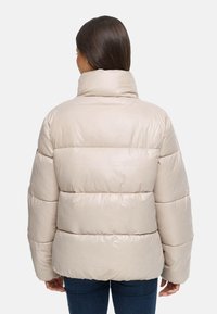 Giubbotto imbottito beige con colletto alto, polsini a coste e una finitura liscia e lucida. Forma squadrata con trapuntatura orizzontale e vestibilità comoda.