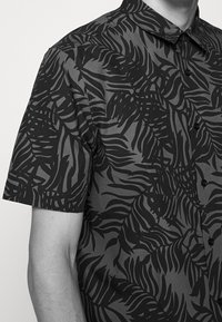 Korte mouw knoopshirt met een zwart en donkergrijs bladpatroon, afgewerkt met een spread collar en zwarte knopen. Zachte stoftextuur.