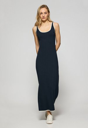 Navy ribbed maxi dress with white trim, featuring a scoop neckline and spaghetti straps, paired with white sneakers.