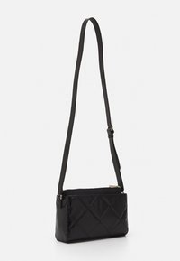 Sort rektangulær crossbody taske med justerbar rem, kviltet mønster og lynlåslukning på en hvid baggrund.
