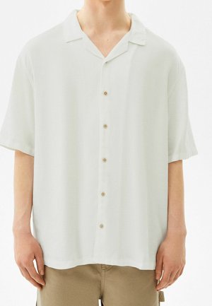 Chemise à manches courtes, verte claire, avec un tissu lisse. Caractéristiques : un col en V et six boutons crème sur le devant.