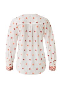 Camicia bianca a maniche lunghe con motivi a diamante in arancione e rosso. Polsini decorati con dettagli intricati. Tessuto leggero con una texture morbida.