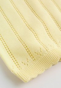 Tissu tricoté jaune avec des côtes verticales et des motifs ajourés. Le bord inférieur présente une finition en feston pour une touche de détail supplémentaire.