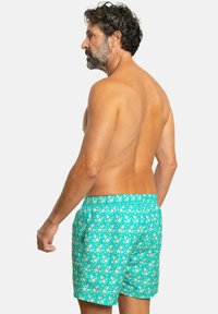 Bañadores de hombre en color turquesa con un patrón de estrellas. Cuentan con una cinturilla elástica y bolsillos laterales. El material parece ligero y de secado rápido.