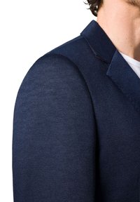 Granatowa marynarka wykonana z teksturowanej tkaniny, z wyraźnymi ramionami i wykładanym kołnierzem z detalami w szwie.