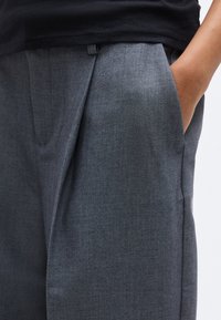 Γκρι ραμμένο παντελόνι με υφασμάτινη υφή, που διαθέτει πιέτα μπροστά και πλαϊνές τσέπες. Η γραμμή είναι ελαφρώς φαρδιά στη μέση.