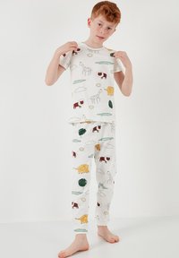 Valkoinen puuvillapijama-setti, jossa on leikkisiä eläin- ja pilvikuoseja eri väreissä. Lyhythihainen paita ja siihen sopivat pitkät housut. Kevyt rakenne.