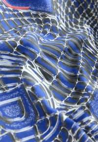 Zils audums ar strukturētu melno un balto viļņu un līniju rakstu, veidojot viļņainu dizainu. Gluda tekstūra ar dzīvīgām krāsām.