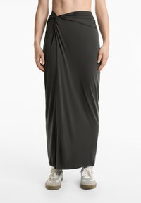 Gonna maxi grigio scuro in tessuto liscio, con un design anteriore attorcigliato e uno spacco laterale, abbinata a sneakers chiare.