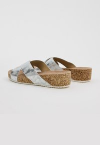 Sandalias de plataforma de corcho con tiras cruzadas de plata y gris con patrón. Superficie texturizada, tacón elevado y suela de goma de color claro.