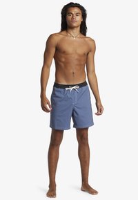 Blaue Badehose aus leichtem Material; schwarzer Bund mit weißem Kordelzug; flache Nähte; knielange Schnittform.