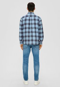 Camicia a scacchi nei toni del blu, nero e bianco, con colletto button-down. Presenta maniche lunghe e orlo dritto. Abbinata a jeans azzurri chiari.