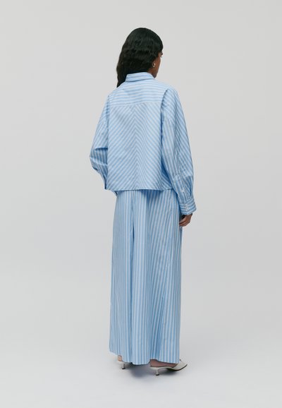 Camicia oversize a righe blu e bianche con un taglio squadrato, abbinata a pantaloni larghi coordinati, entrambi con una vestibilità comoda e dettagli con bottoni.