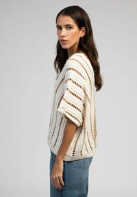 Pull crème à rayures, en tricot ouvert, à manches courtes, coupe décontractée et motif texturé. Porté avec un jean bleu.