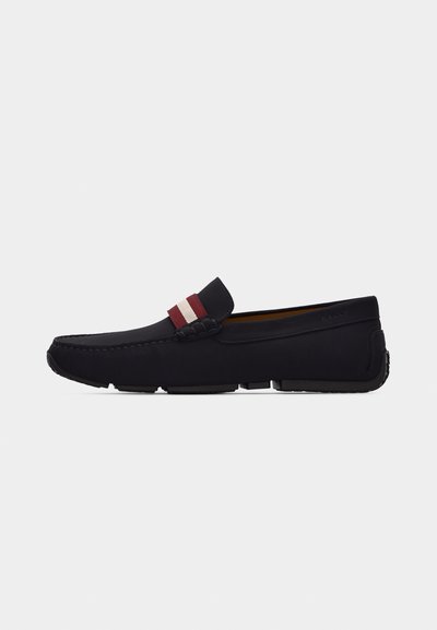 Mocassin en cuir noir avec une bande en tissu rouge et blanc sur le dessus et une semelle en caoutchouc segmentée, vu de profil.