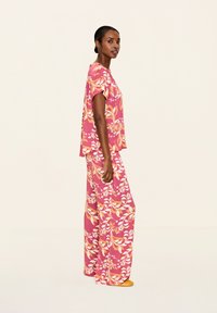 Completo due pezzi con motivo floreale rosa, composto da una blusa ampia a maniche corte e pantaloni a gamba larga, realizzato in tessuto leggero e testurizzato.