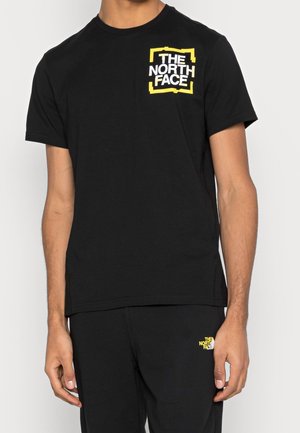 Person iført sort t-shirt med korte ærmer og bukser med gule og hvide "The North Face" logoer på brystet og låret.