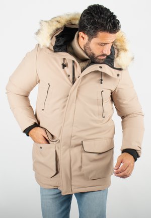 Parka beige isolée avec une capuche doublée de fausse fourrure, des fermetures éclair à l'avant et de grandes poches à rabat. Accents noirs aux poignets et à la doublure.
